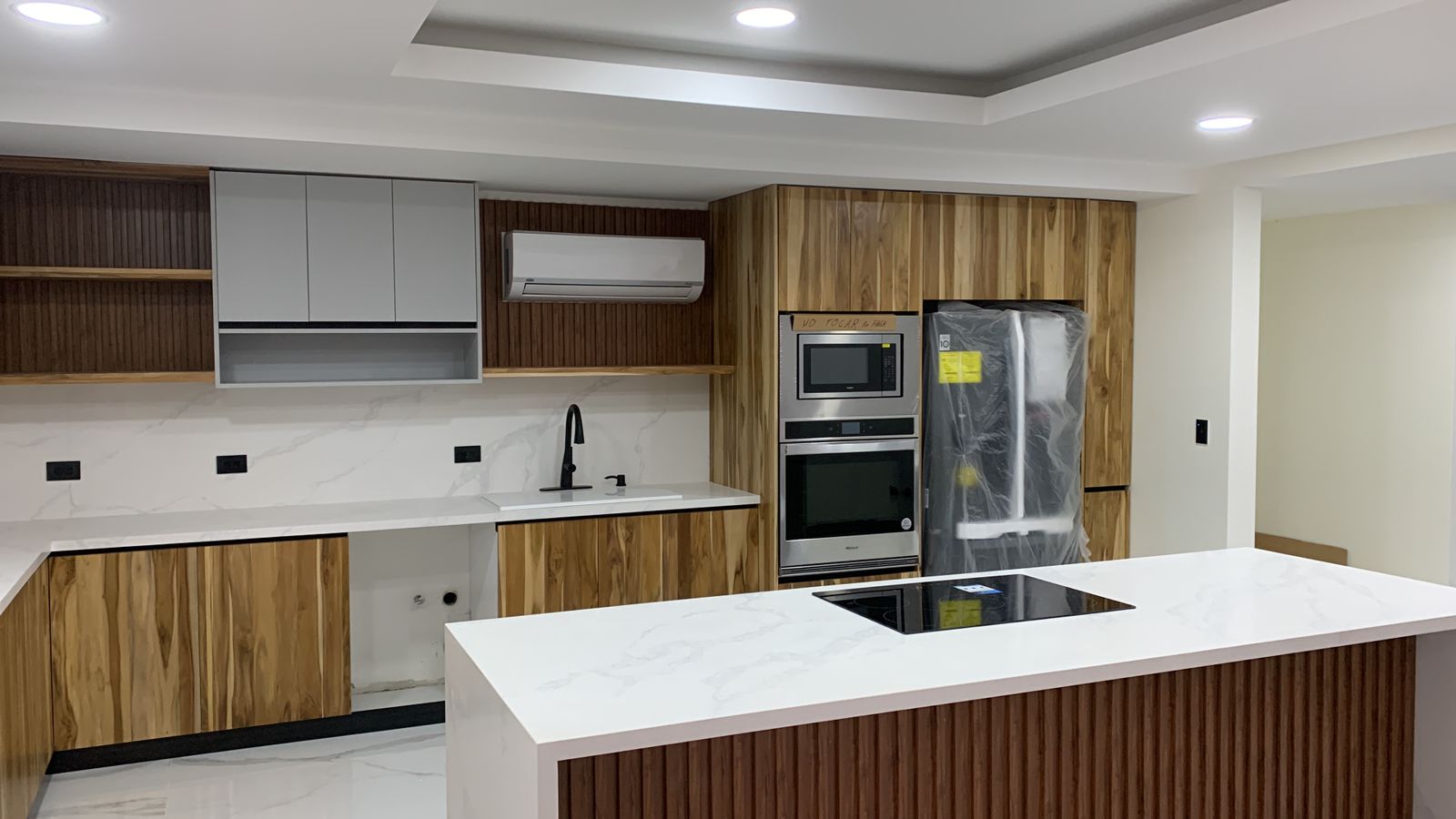 Cocina contemporánea con isla blanca, paneles en madera natural y electrodomésticos empotrados.